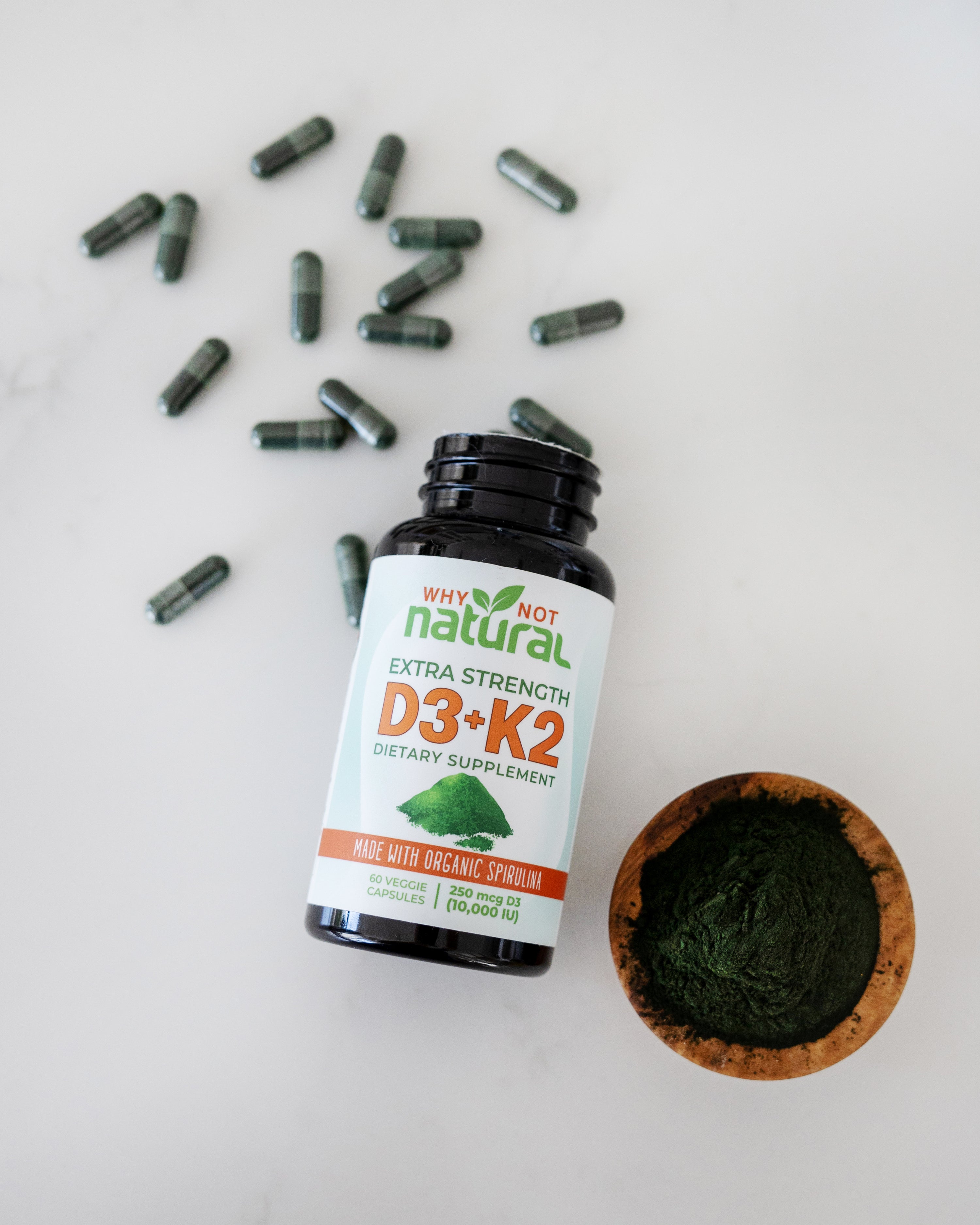 Bottle of vitamin D3-K2 on counter with capsules around it and bowl of spirulina.