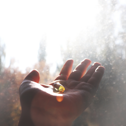 A person holding a vitamin D pill in front of a window, with sunlight streaming through.