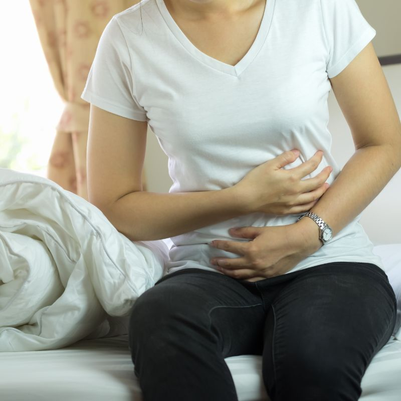 A woman sitting on a bed, holding her stomach in pain.