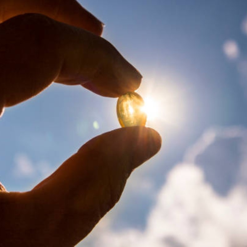 A person holding up a vitamin pill with sunlight streaming through it