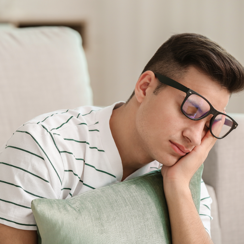 A sleepy man with glasses resting on a couch, lacking energy.