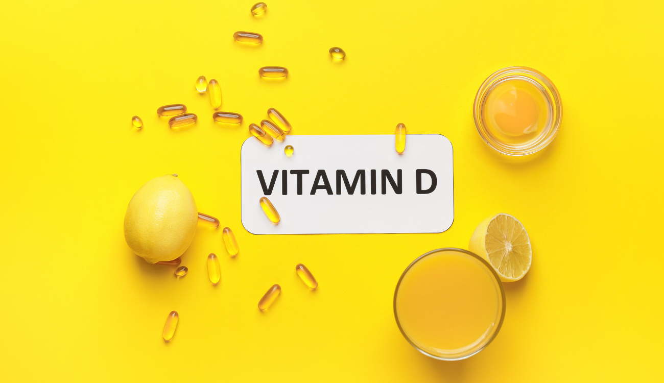 Vitamin D supplements and lemon juice displayed on a vibrant yellow surface.