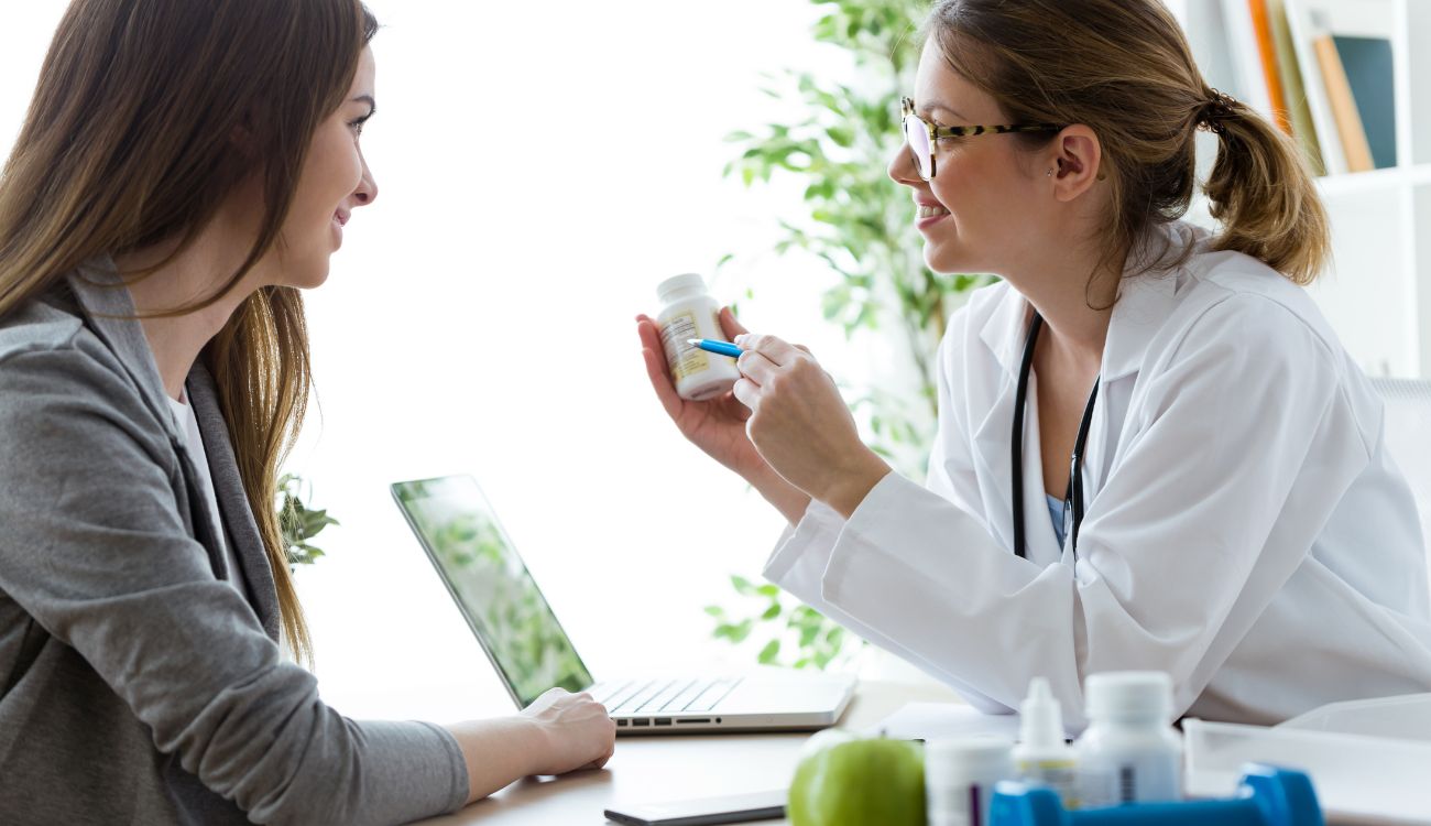 A woman is seated at a desk, conversing with a doctor about her health and treatment options